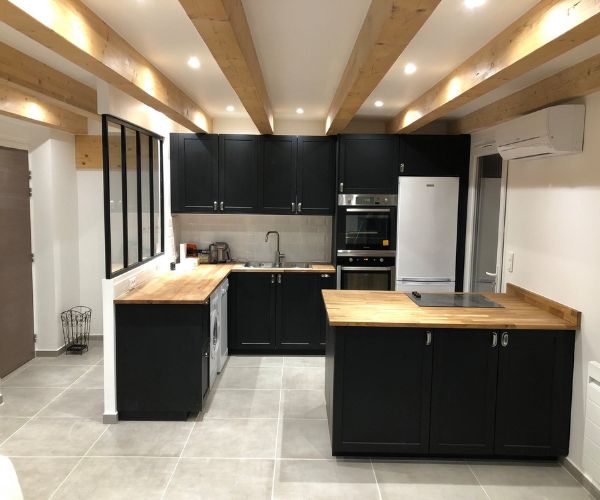 Cuisine rénovée tendance avec meubles noirs, plan bois, verrière et poutres apparentes