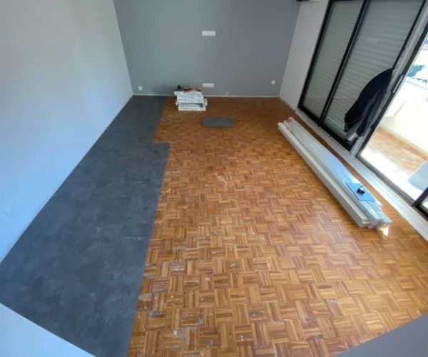 Pose en cours de dalles PVC effet béton sur ancien parquet