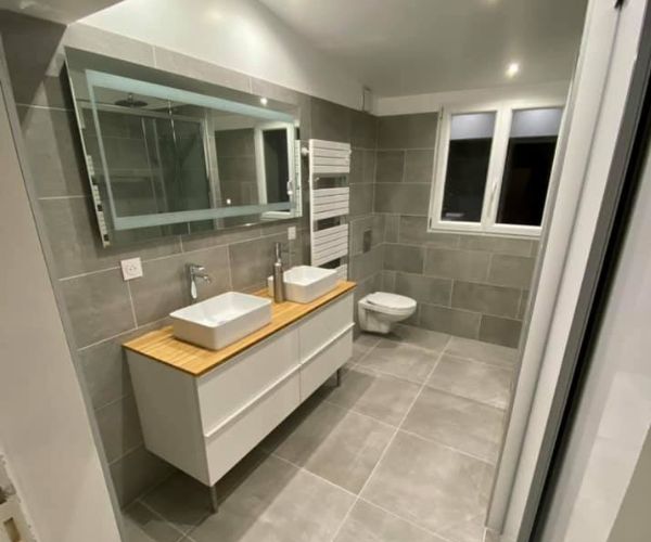 Salle de bain rénovée avec carrelage gris, double vasque et WC suspendu