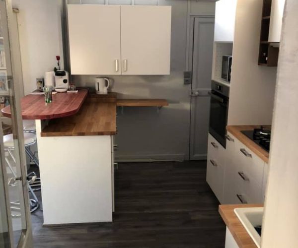 Vue arrière d’une cuisine rénovée avec meubles blancs et plan bois