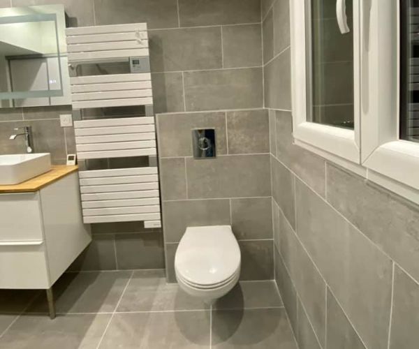 WC suspendu installé dans une salle de bain rénovée avec carrelage gris